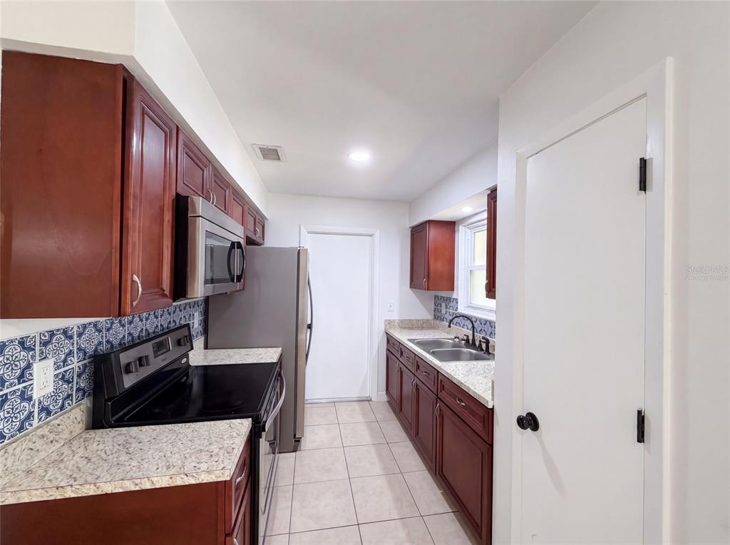 A kitchen features dark wood cabinets, granite countertops, a blue patterned backsplash, and tile flooring — 7233 THOMAS JEFFERSON CIRCLE W, BARTOW, FL