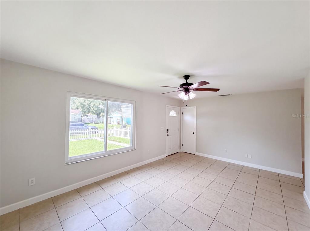 A living room with light-colored walls, tile flooring, a ceiling fan, and a large window — 7233 THOMAS JEFFERSON CIRCLE W, BARTOW, FL