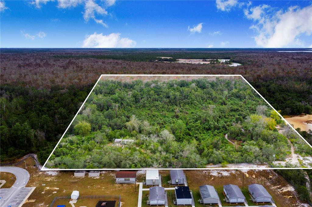 An aerial view shows a large, wooded plot of land outlined in white behind houses — LAUREL AVENUE, POINCIANA, FL