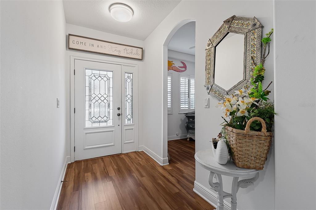 A bright entryway features wood-look flooring, a white front door, and a decorative wall mirror — 50 PALM HARBOR PARKWAY UNIT 38, PALM COAST, FL