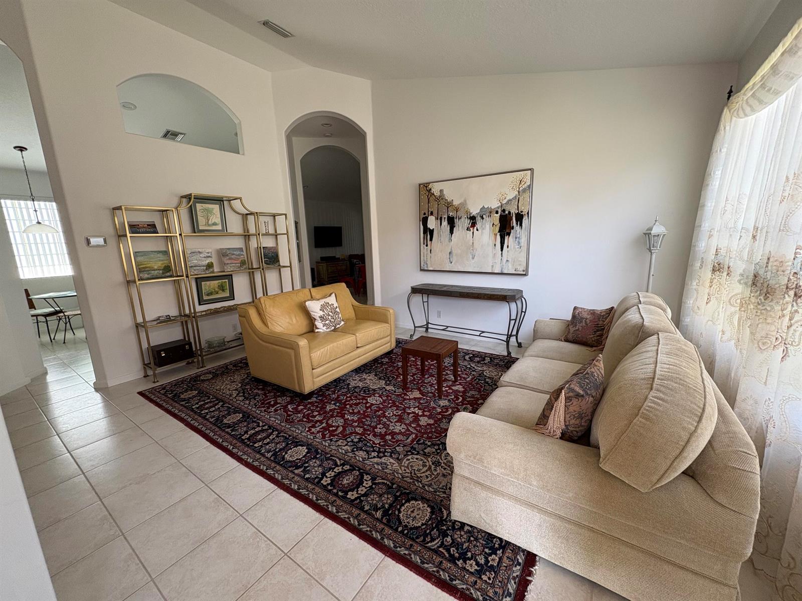 A living room with a large patterned rug, two sofas, a gold shelving unit, and artwork — 15426 Fiorenza Circle, Delray Beach FL 33446, DELRAY BEACH, FL