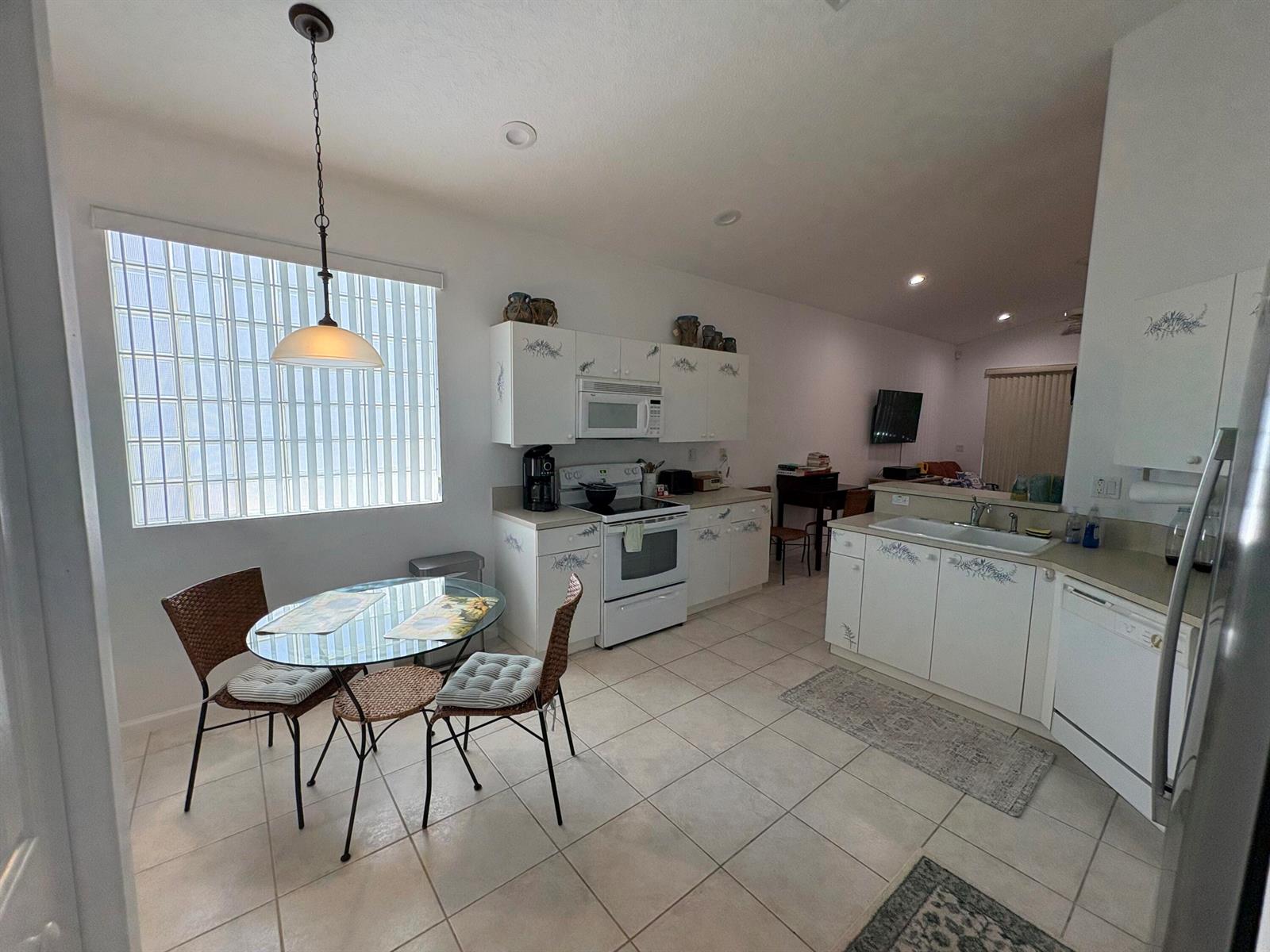 A kitchen with white cabinets, tile flooring, and a small glass dining table near a window — 15426 Fiorenza Circle, Delray Beach FL 33446, DELRAY BEACH, FL