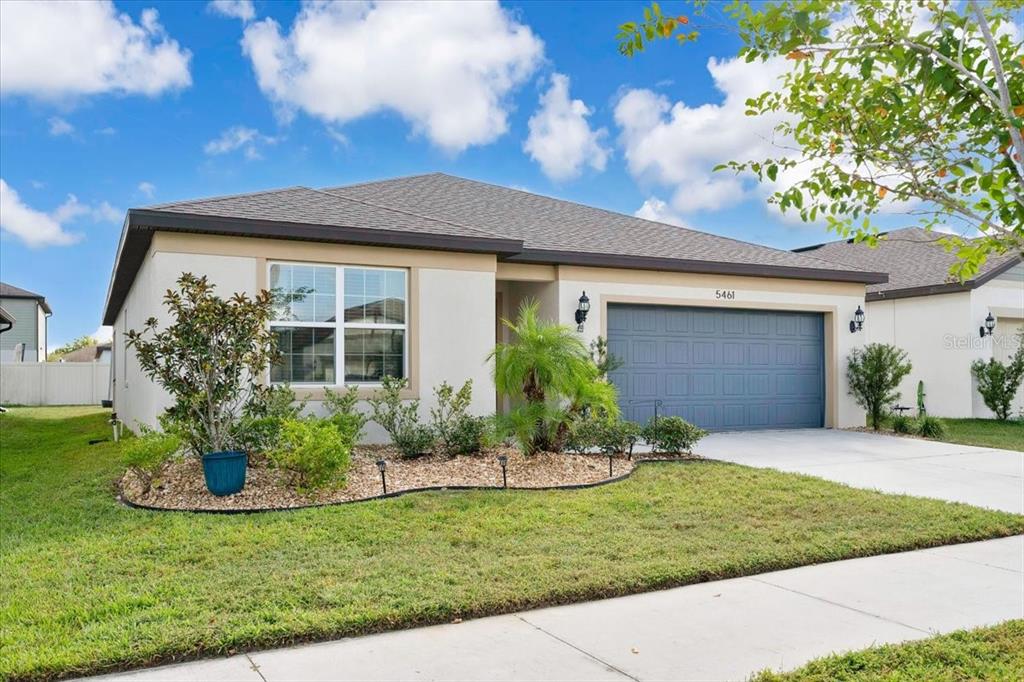 A single-story house with a beige stucco exterior, a two-car garage, and front landscaping — 5461 KEATON SPRINGS DRIVE, LAKELAND, FL
