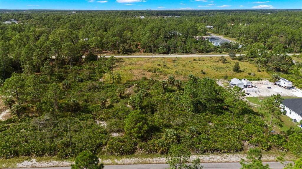 An aerial view of a vacant, wooded lot bordered by a road and nearby houses — 1217 MAGNOLIA AVENUE, LEHIGH ACRES, FL