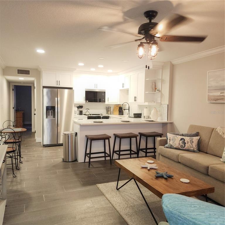 An open-concept kitchen and living area features white cabinetry, stainless steel appliances, and wood-look flooring — 8535 BLIND PASS DRIVE UNIT 103, TREASURE ISLAND, FL