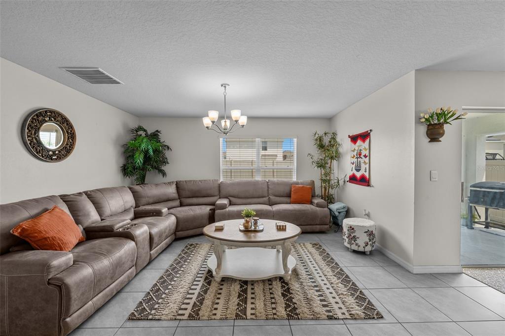 A living room features a large brown sectional sofa, a round coffee table, and tile flooring — 16742 SUNBURST LAKE STREET, WIMAUMA, FL