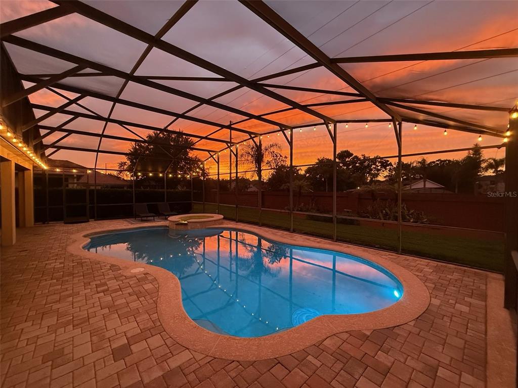 A swimming pool with a spa is enclosed by a screened lanai at sunset — 2759 MARIA ISABEL AVENUE, OCOEE, FL
