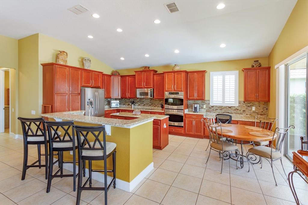 A kitchen features wood cabinets, granite countertops, a breakfast bar with stools, and a dining area — 2759 MARIA ISABEL AVENUE, OCOEE, FL