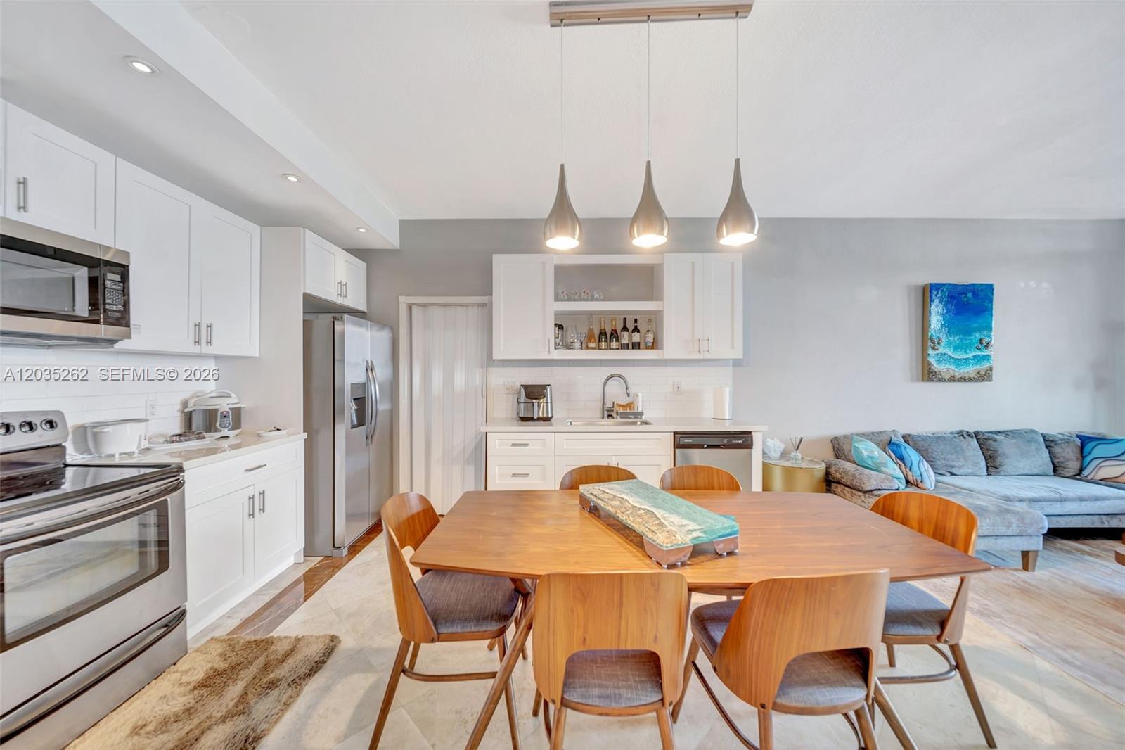 A kitchen and dining area features white cabinetry, stainless steel appliances, and a wooden table — 5005 Collins Ave, Miami Beach FL 33140, MIAMI BEACH, FL