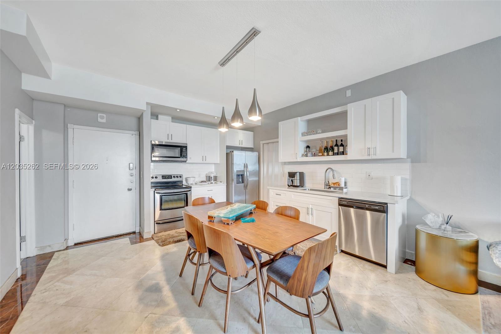 A kitchen features white cabinetry, stainless steel appliances, and a wooden dining table with chairs — 5005 Collins Ave, Miami Beach FL 33140, MIAMI BEACH, FL