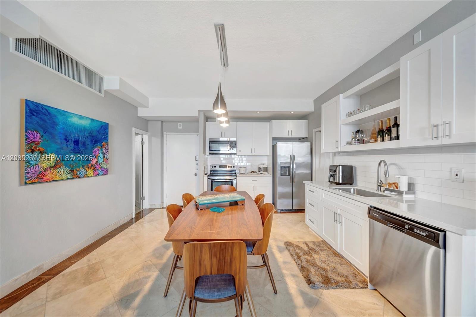 A kitchen and dining area features white cabinets, stainless steel appliances, and a wooden table — 5005 Collins Ave, Miami Beach FL 33140, MIAMI BEACH, FL