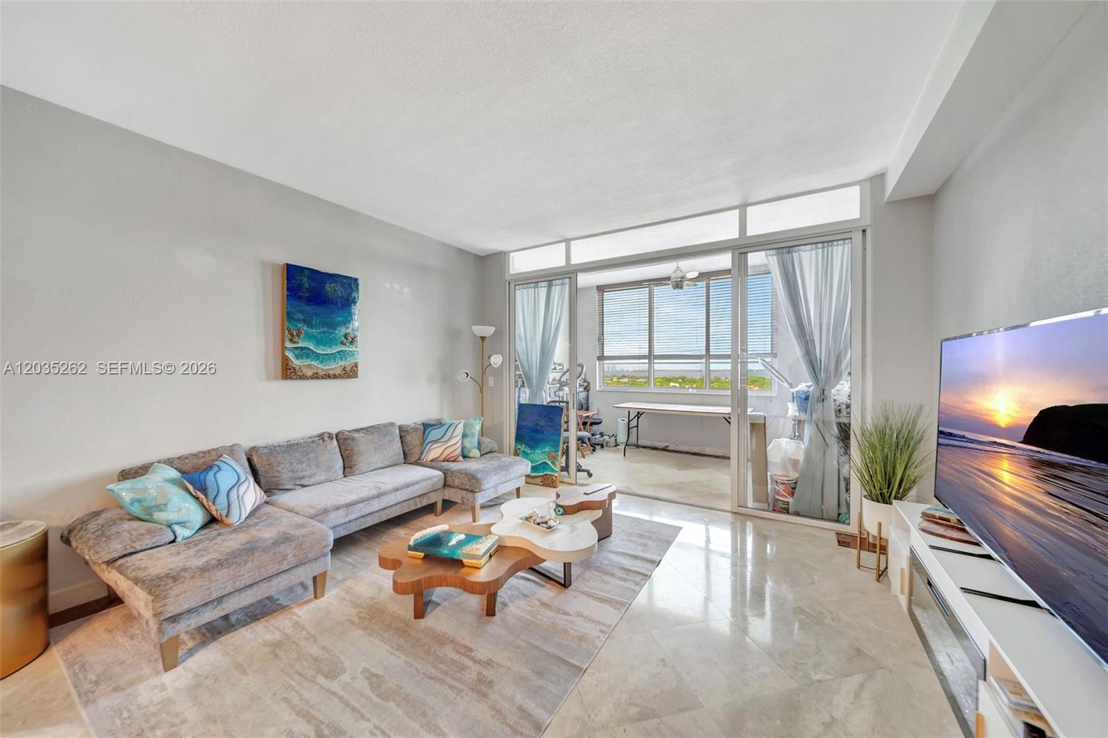 A living room features a gray sectional sofa, coffee tables, and a balcony with views — 5005 Collins Ave, Miami Beach FL 33140, MIAMI BEACH, FL