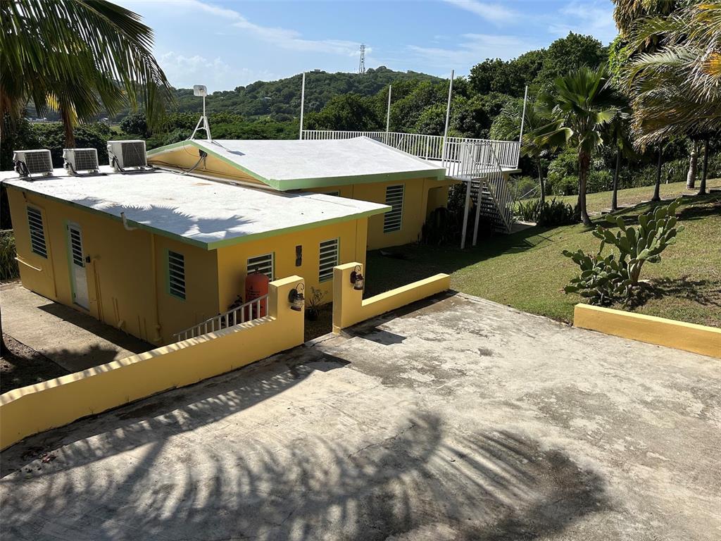 A yellow house with a flat roof, rooftop deck, and concrete driveway sits on a hill — Number 28 DESTINO, VIEQUES, PR