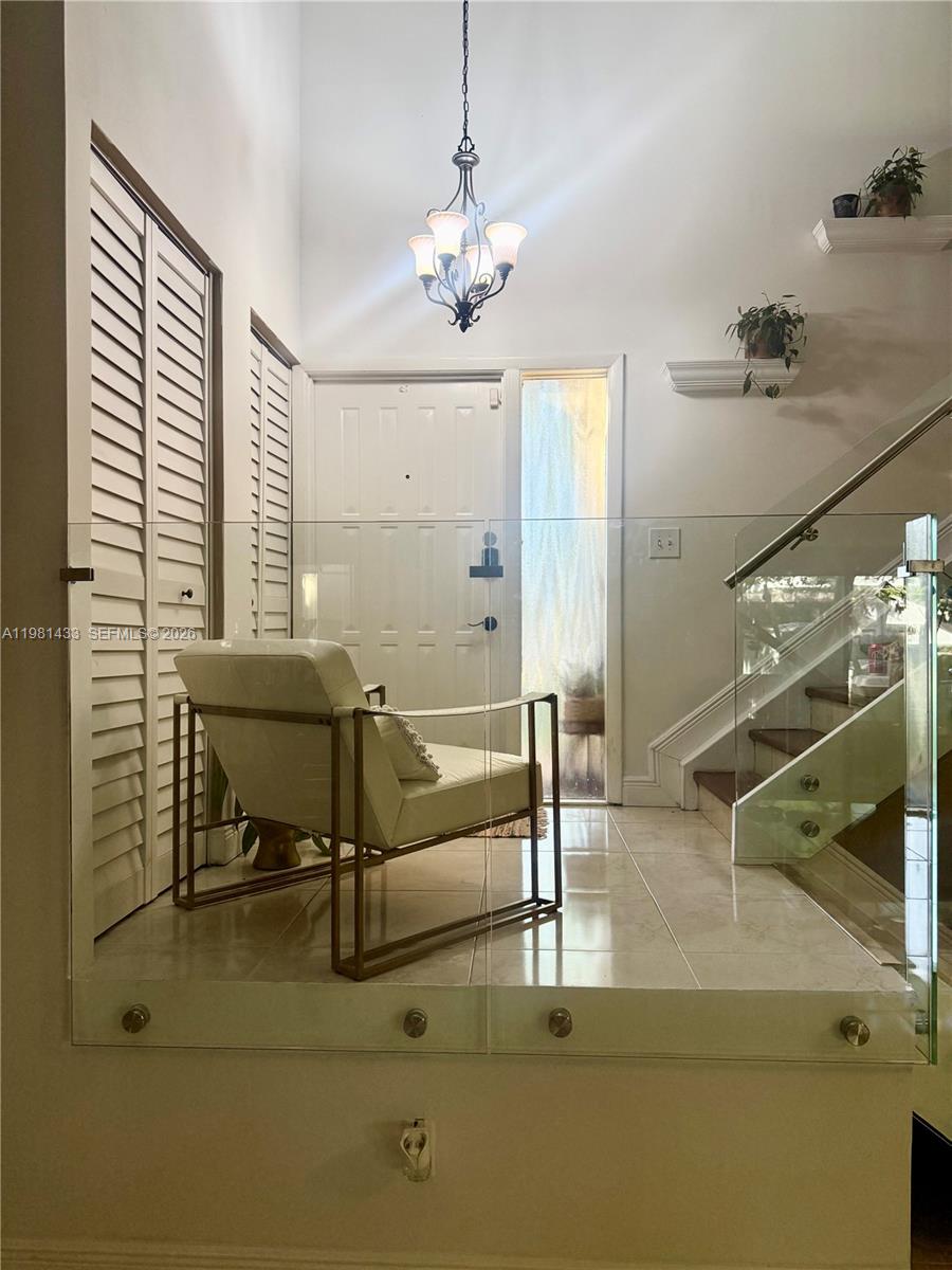 A modern entryway features a glass railing, a white armchair, and a chandelier — 5119 SW 153rd Pl N, Miami FL 33185, MIAMI, FL