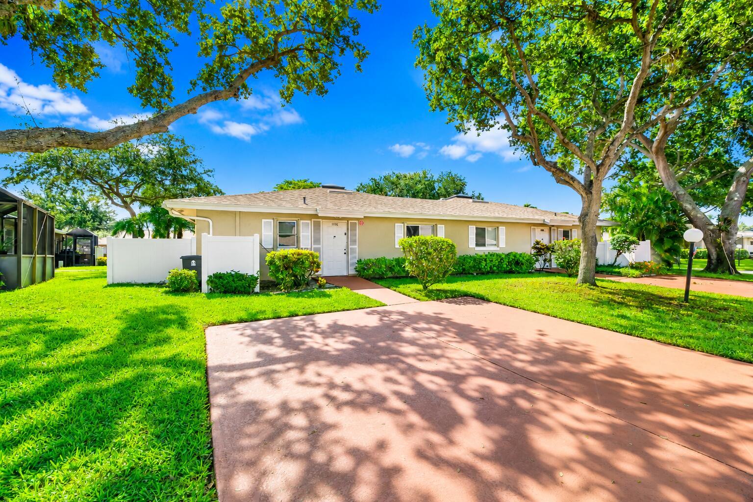 A single-story tan house with a red driveway, white shutters, and mature trees in front — 18762 Candlewick Drive, Boca Raton FL 33496, BOCA RATON, FL