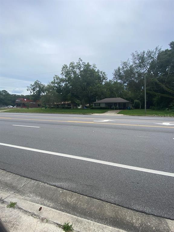 A single-story house sits behind a large, multi-lane road with mature trees in the background — 24809 W NEWBERRY ROAD, NEWBERRY, FL