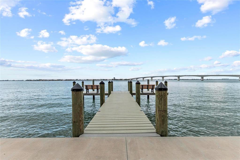 A wooden dock extends into a bay toward a distant bridge under a cloudy sky — 350 GOLDEN GATE POINT UNIT 61, SARASOTA, FL