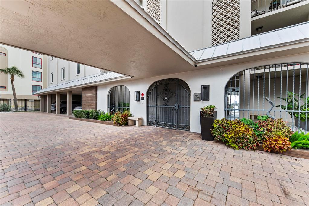 A paved driveway leads to a gated entrance beneath a covered building overhang — 350 GOLDEN GATE POINT UNIT 61, SARASOTA, FL