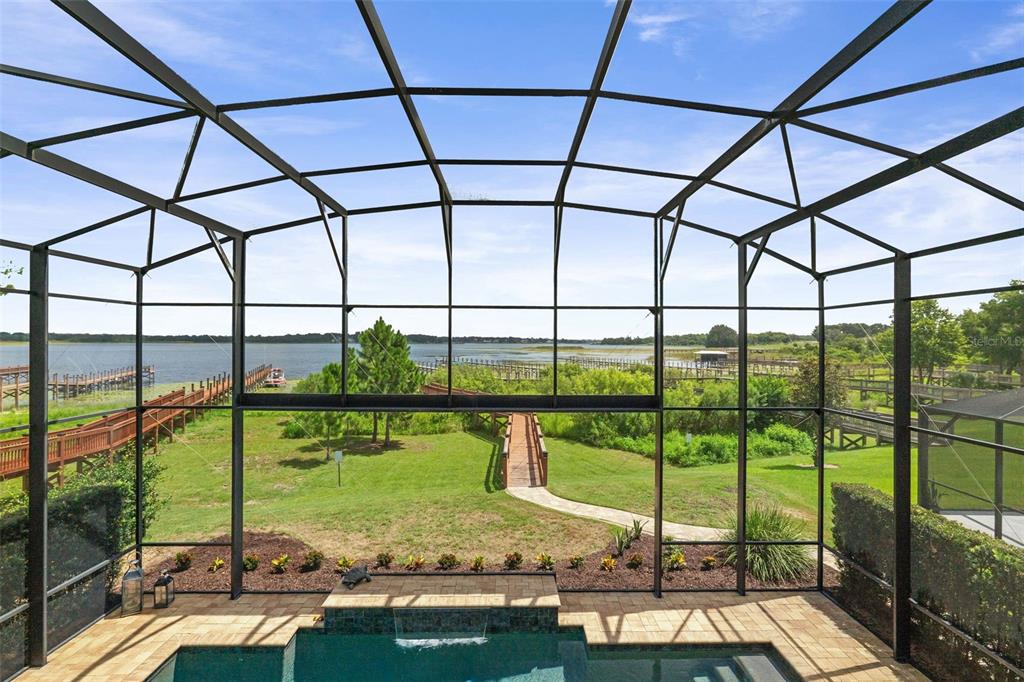 A screened-in pool patio overlooks a grassy lawn, a wooden walkway, and a large lake — 3462 SHALLOW COVE LANE, CLERMONT, FL