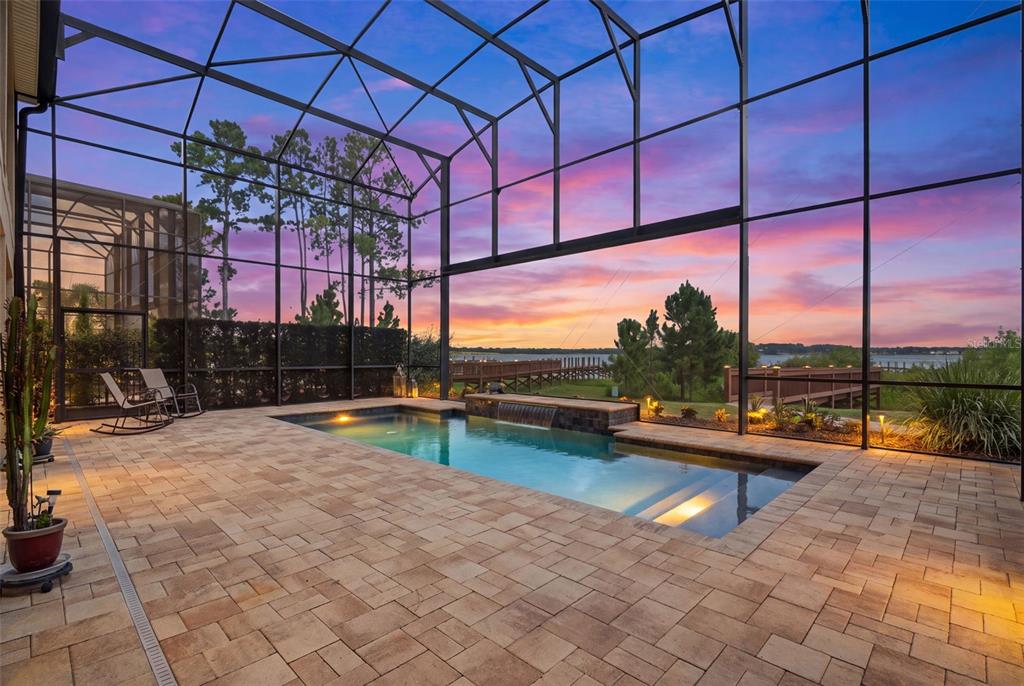 A screened-in patio features a rectangular swimming pool with a water feature and sunset views — 3462 SHALLOW COVE LANE, CLERMONT, FL