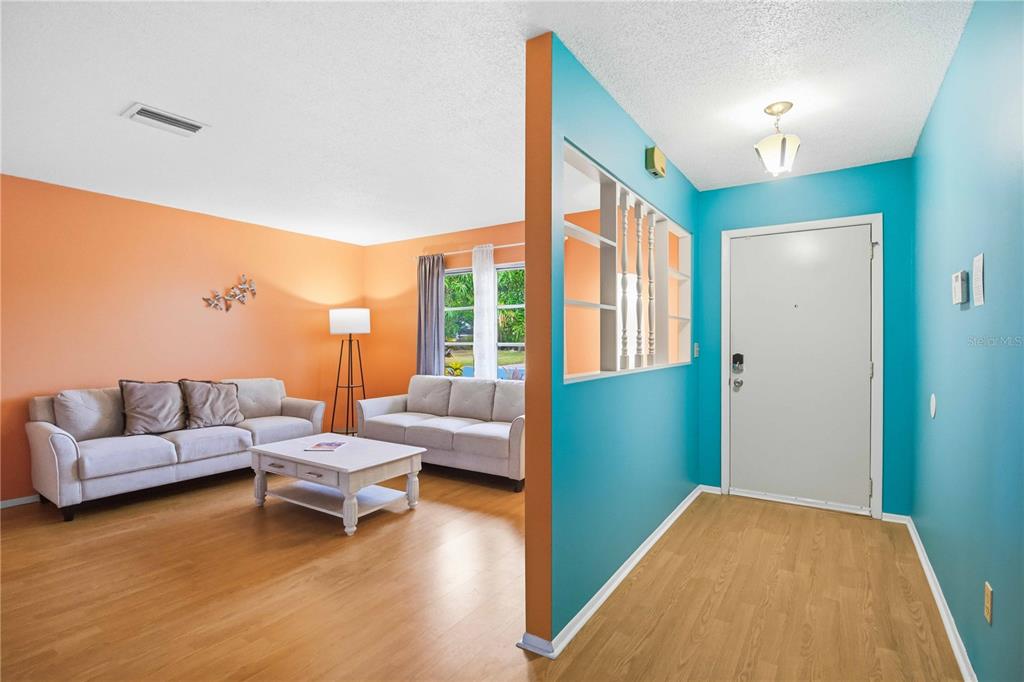 An entryway with blue walls leads into a living room featuring orange walls and sofas — 5203 18TH AVENUE W, BRADENTON, FL