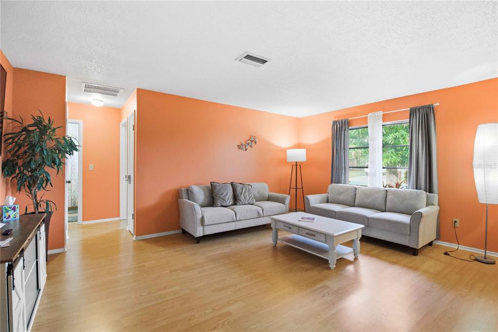 A living room with orange walls, light wood flooring, and two gray sofas — 5203 18TH AVENUE W, BRADENTON, FL