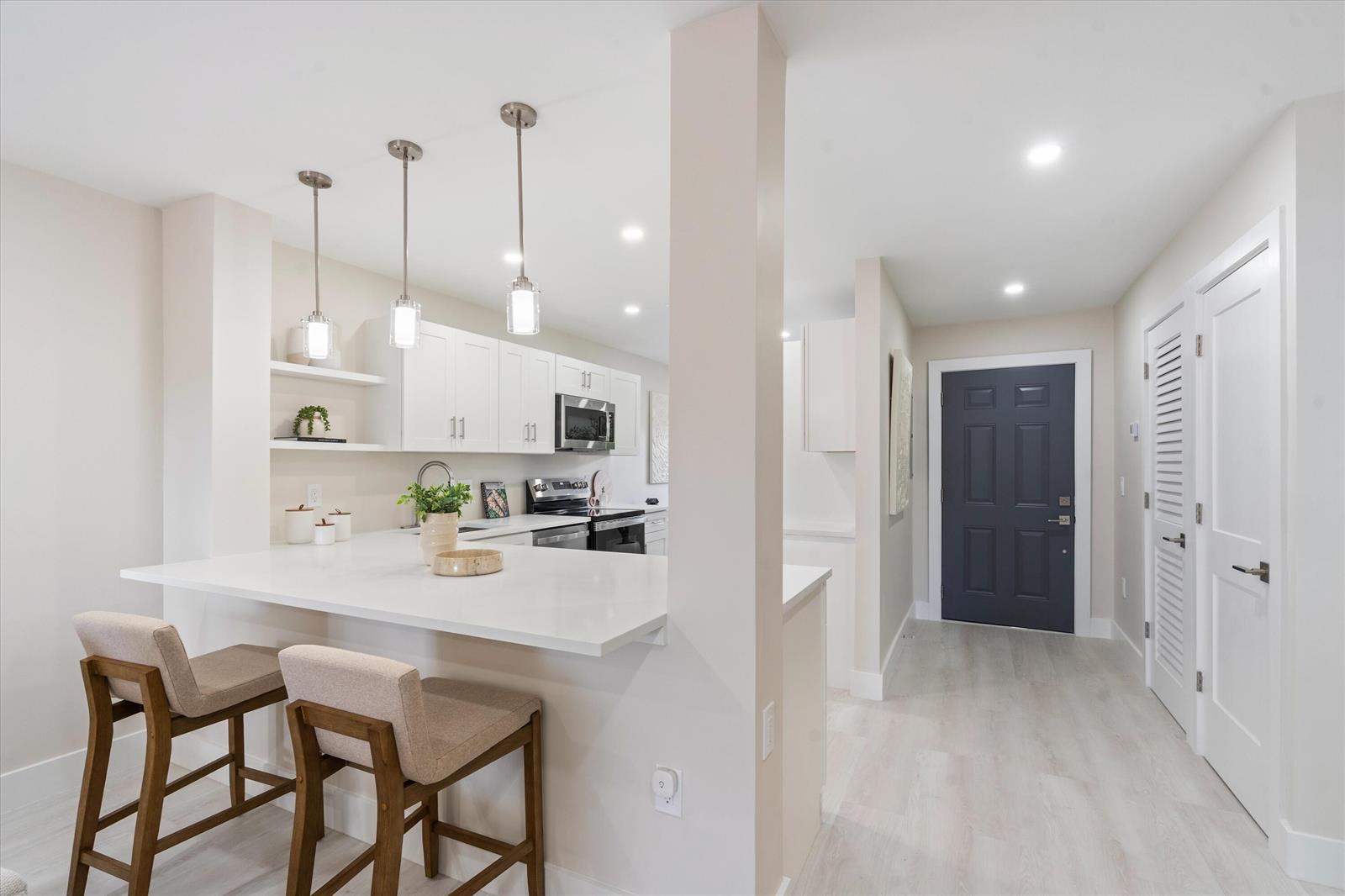 A kitchen with white cabinets and a breakfast bar overlooks a hallway with a door — 47 Stratford Lane W # F, Boynton Beach FL 33436, BOYNTON BEACH, FL