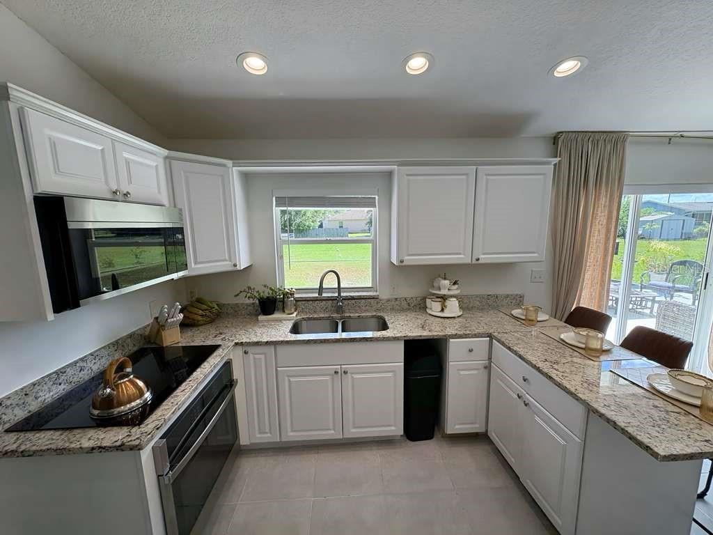 A kitchen with white cabinets, granite countertops, stainless steel appliances, and a view of the backyard — 605 TAMARIN LANE, KISSIMMEE, FL