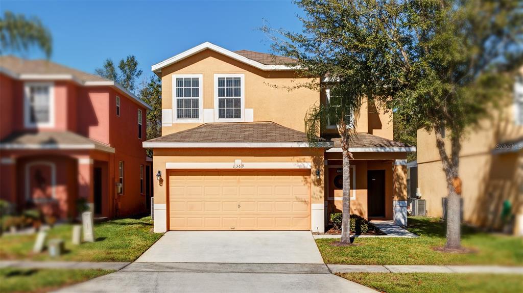 A two-story house with a tan stucco exterior, a two-car garage, and a concrete driveway — 1369 ROYAL RIDGE DRIVE, DAVENPORT, FL