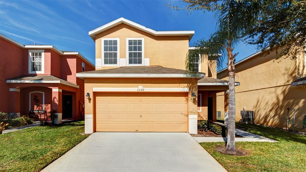 A two-story, orange-stucco house with a two-car garage and a palm tree in front — 1369 ROYAL RIDGE DRIVE, DAVENPORT, FL