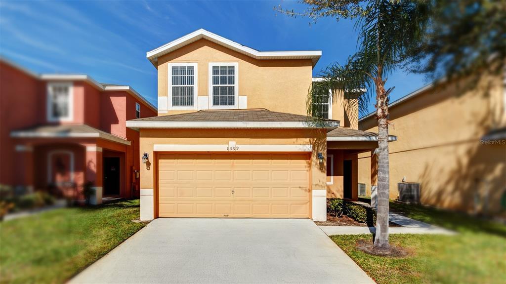 A two-story, tan-colored suburban house features a two-car garage and a paved driveway — 1369 ROYAL RIDGE DRIVE, DAVENPORT, FL
