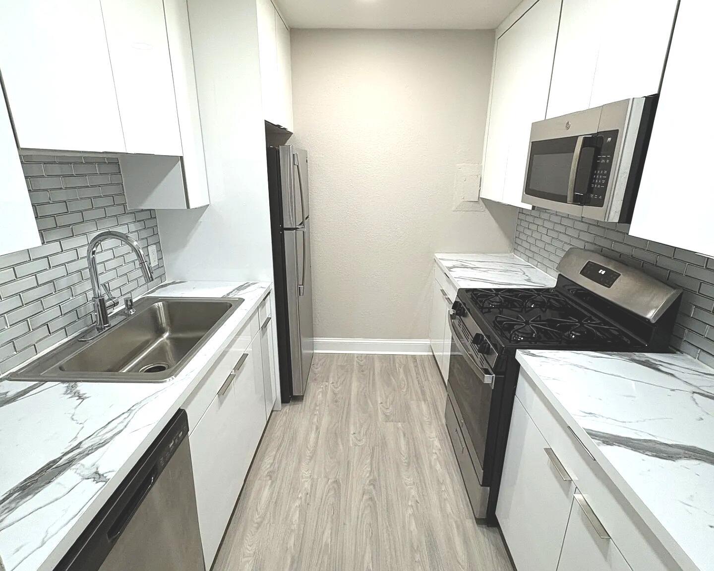 A galley kitchen features white cabinets, marble-patterned countertops, stainless steel appliances, and gray subway tile — 601 SW 2nd Avenue # 5, Boca Raton FL 33432, BOCA RATON, FL