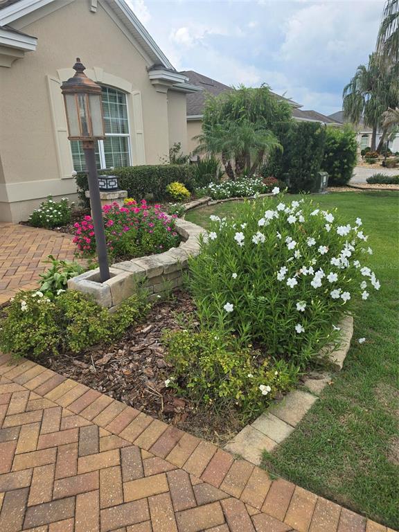 A brick walkway leads to a landscaped garden bed with a lamp post and flowers — 3452 BOSIE RUN, THE VILLAGES, FL