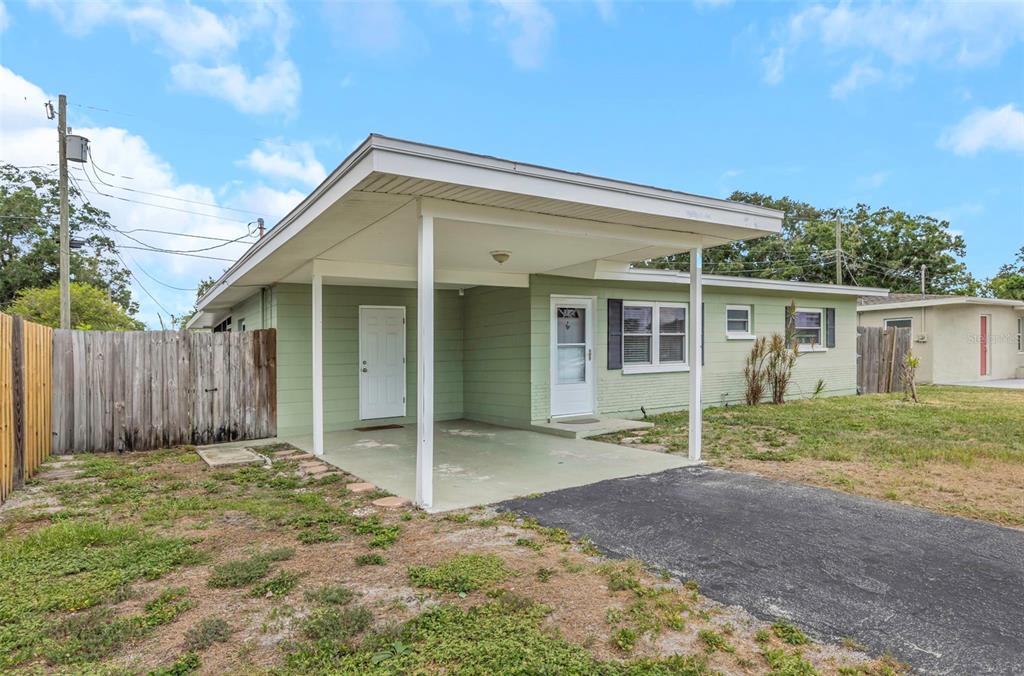 A light green house with a carport, a paved driveway, and a wooden privacy fence — 5711 92ND AVENUE N, PINELLAS PARK, FL
