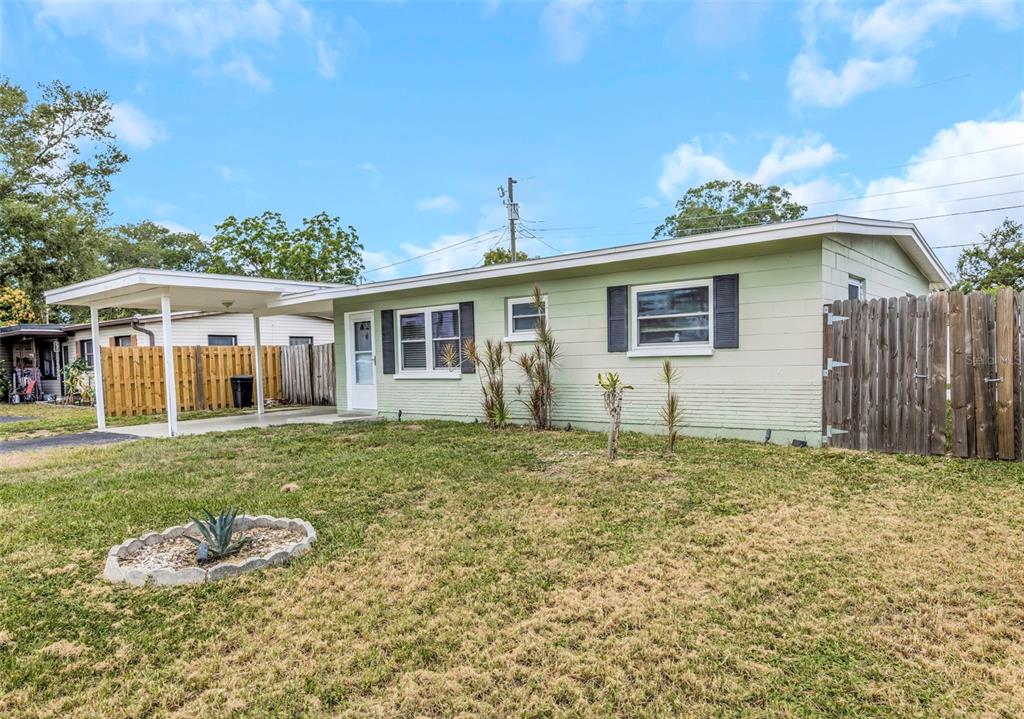 A light green single-story house features a carport, a front lawn, and a wooden fence — 5711 92ND AVENUE N, PINELLAS PARK, FL