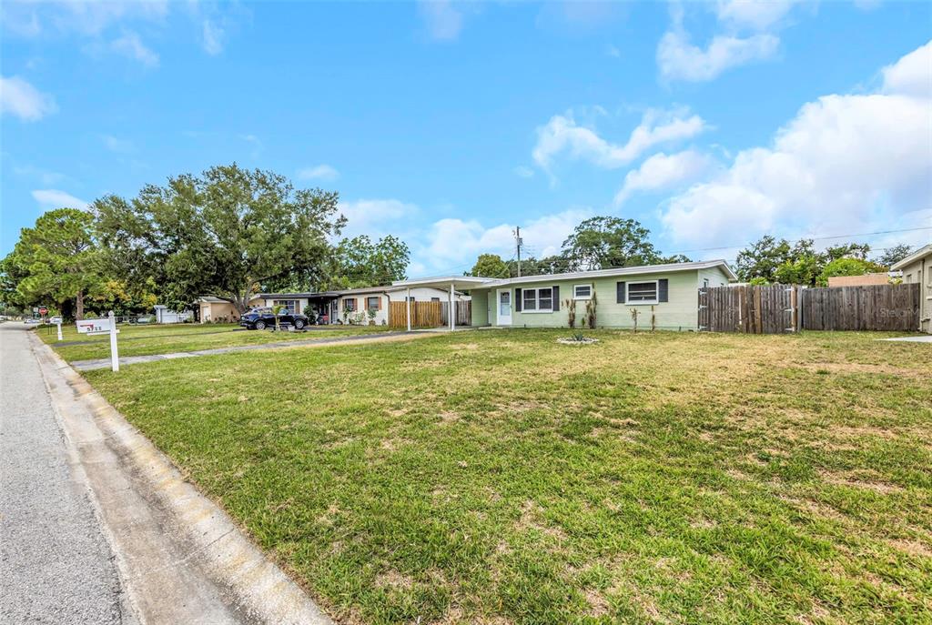A light green single-story house with a carport sits on a large grassy lot — 5711 92ND AVENUE N, PINELLAS PARK, FL