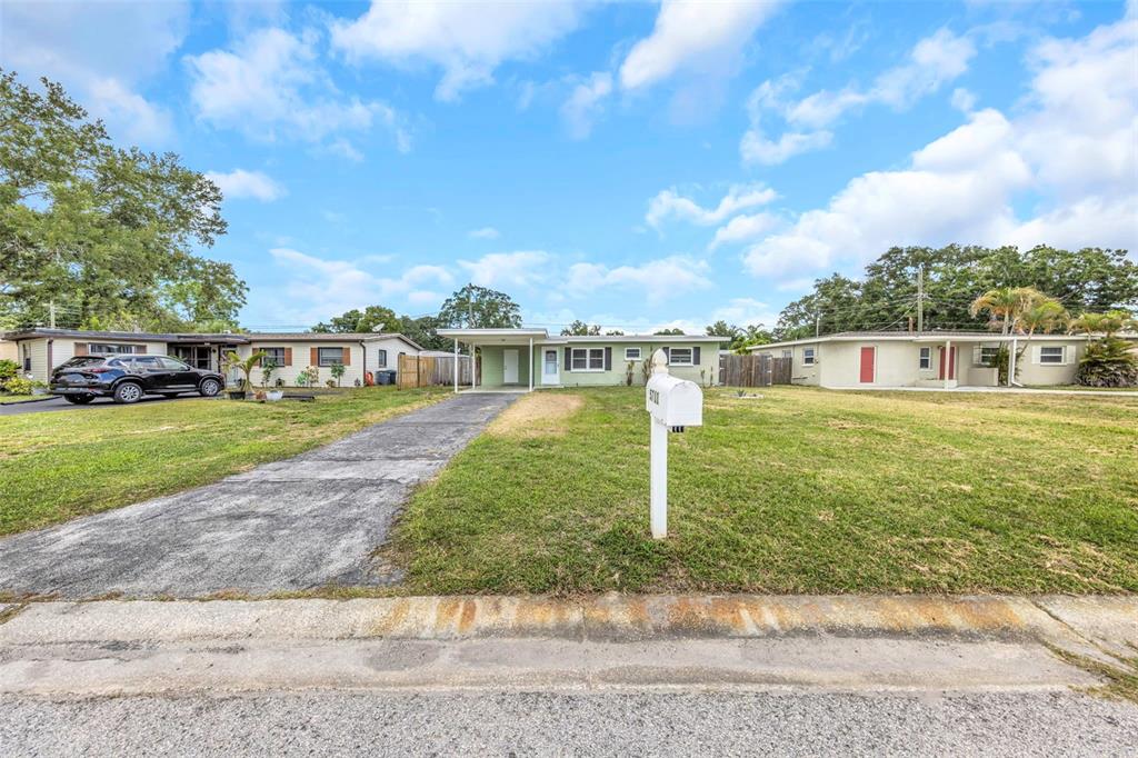 A single-story house with a carport and a paved driveway sits on a grassy lot — 5711 92ND AVENUE N, PINELLAS PARK, FL