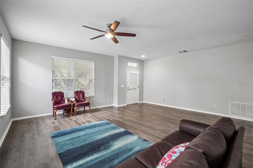 A living room with light gray walls, wood-look flooring, a ceiling fan, and two chairs — 6111 GANNETSIDE PLACE, LITHIA, FL