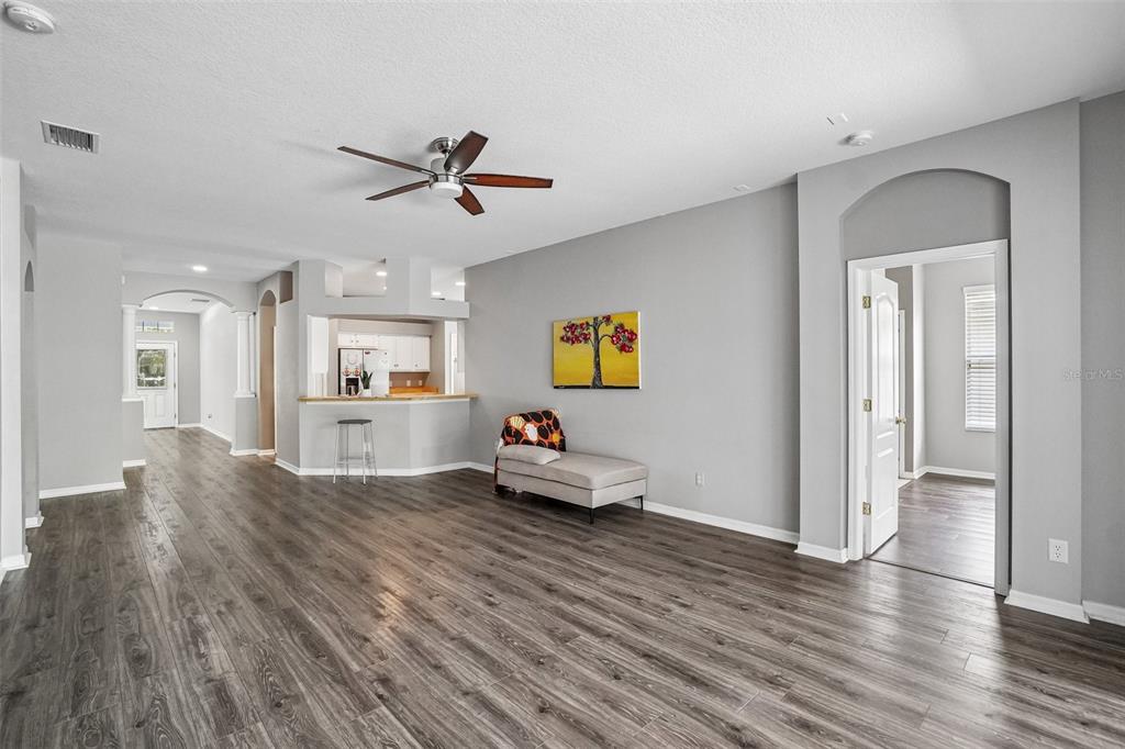 A spacious living room features wood-look flooring, a ceiling fan, and a pass-through kitchen counter — 6111 GANNETSIDE PLACE, LITHIA, FL