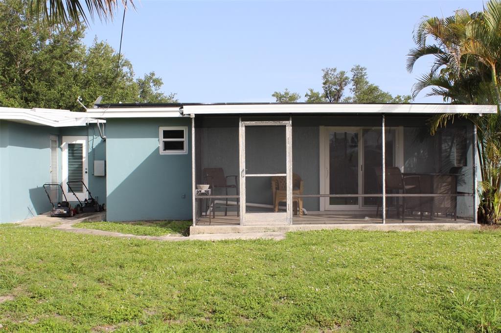 The exterior of a blue house features a screened-in porch and a grassy backyard — 2513 AMBROSE LANE, PORT CHARLOTTE, FL