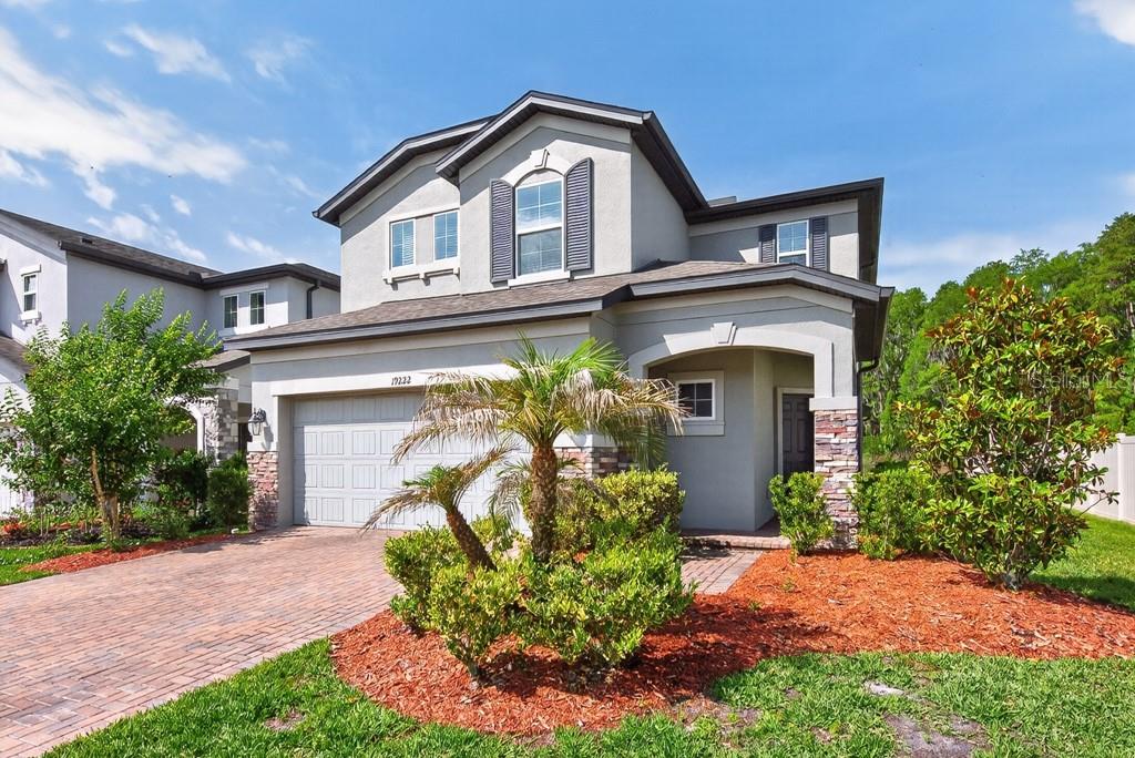 A two-story suburban house features a gray stucco exterior, stone accents, and a brick driveway — 19222 OLD SPANISH ROAD, TAMPA, FL