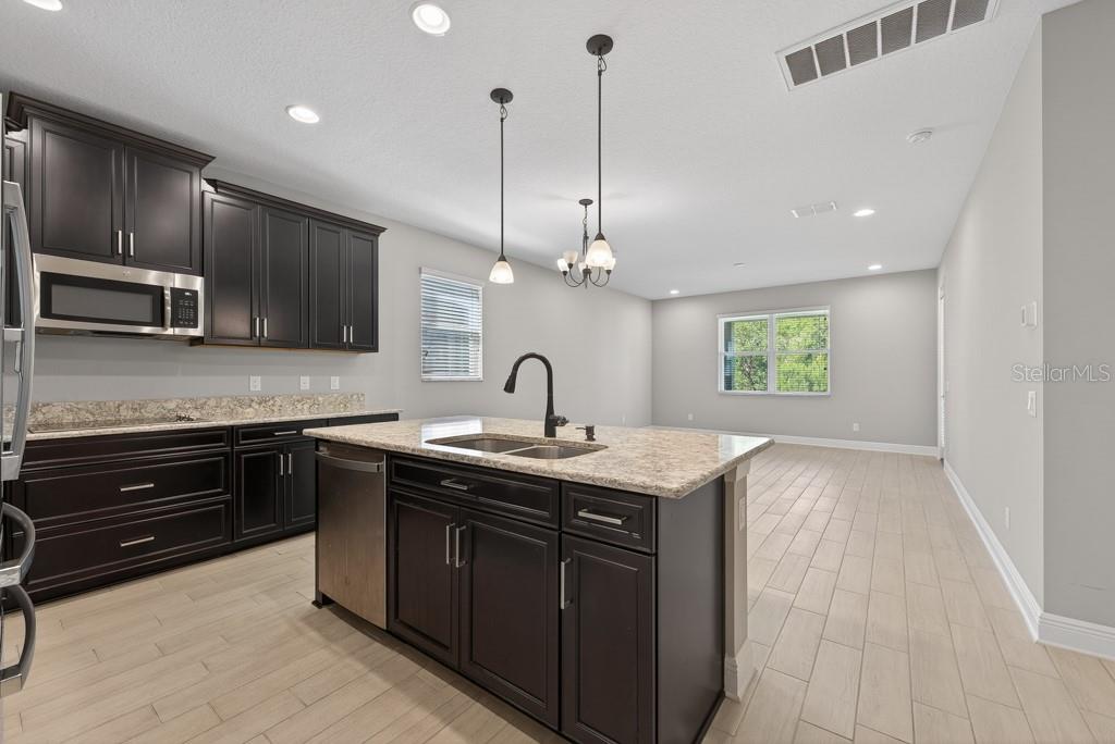 A kitchen features dark wood cabinets, granite countertops, a center island, and light tile flooring — 19222 OLD SPANISH ROAD, TAMPA, FL
