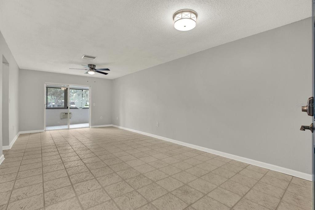 An empty room with light gray walls, tiled flooring, a ceiling fan, and sliding glass doors — 1204 11TH CIRCLE SE, LARGO, FL