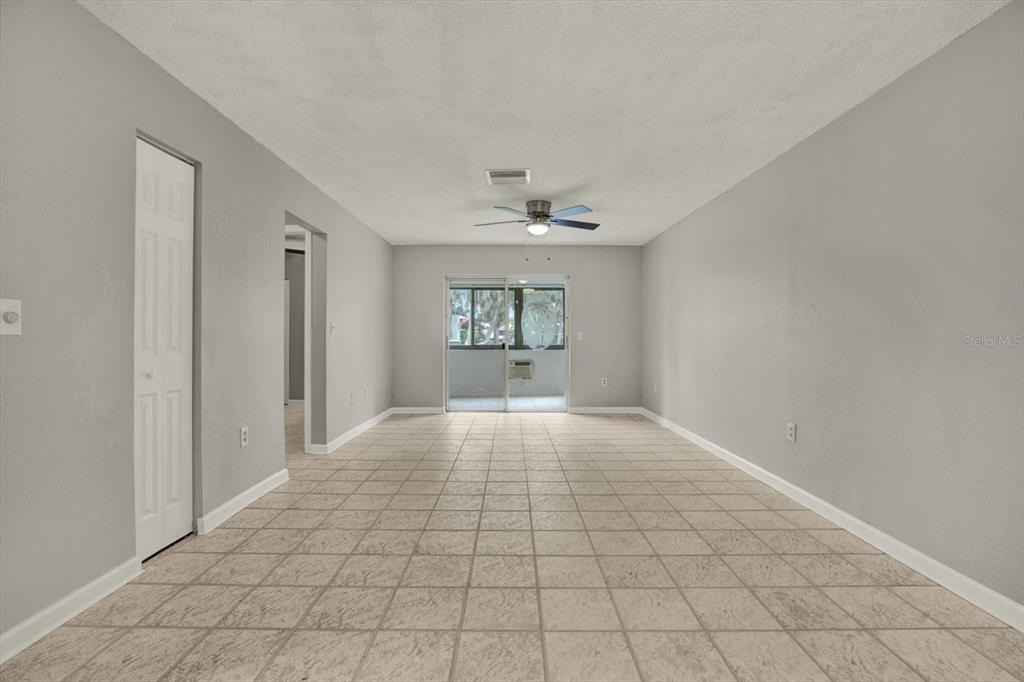 An empty room features light gray walls, beige tile flooring, a ceiling fan, and sliding doors — 1204 11TH CIRCLE SE, LARGO, FL