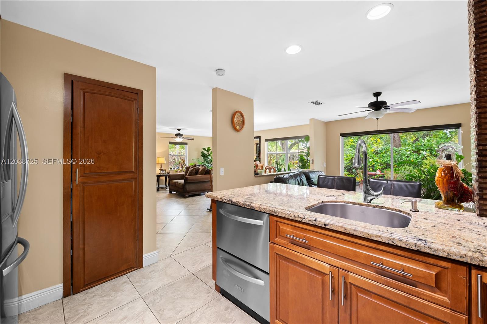A kitchen with granite countertops and wood cabinets overlooks a living room with tile flooring — 2021 Barcelona Ter, Margate FL 33063, MARGATE, FL