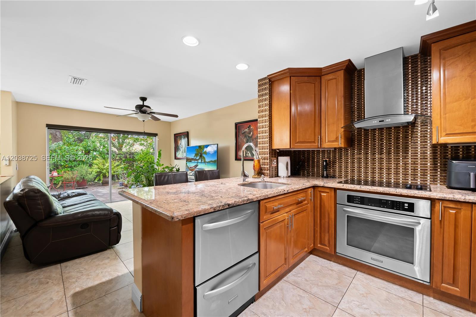 A kitchen with wood cabinets, granite countertops, and stainless steel appliances overlooks a living area — 2021 Barcelona Ter, Margate FL 33063, MARGATE, FL
