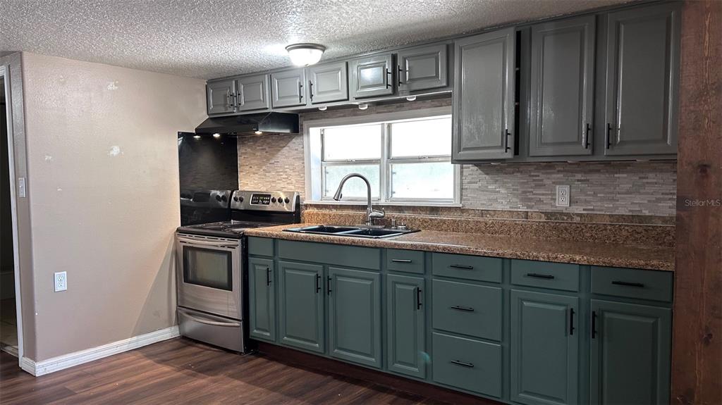 A kitchen features dark green lower cabinets, grey upper cabinets, granite countertops, and stainless appliances — 4800 PETROFF AVENUE, ORLANDO, FL