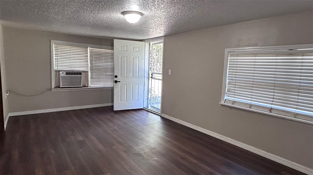 An empty room features dark wood-look flooring, light gray walls, two windows, and an exterior door — 4800 PETROFF AVENUE, ORLANDO, FL