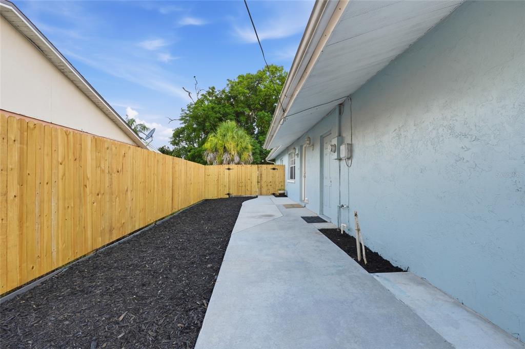 A concrete walkway runs alongside a light blue house exterior next to a wooden fence — 1915 COLLEEN STREET, SARASOTA, FL