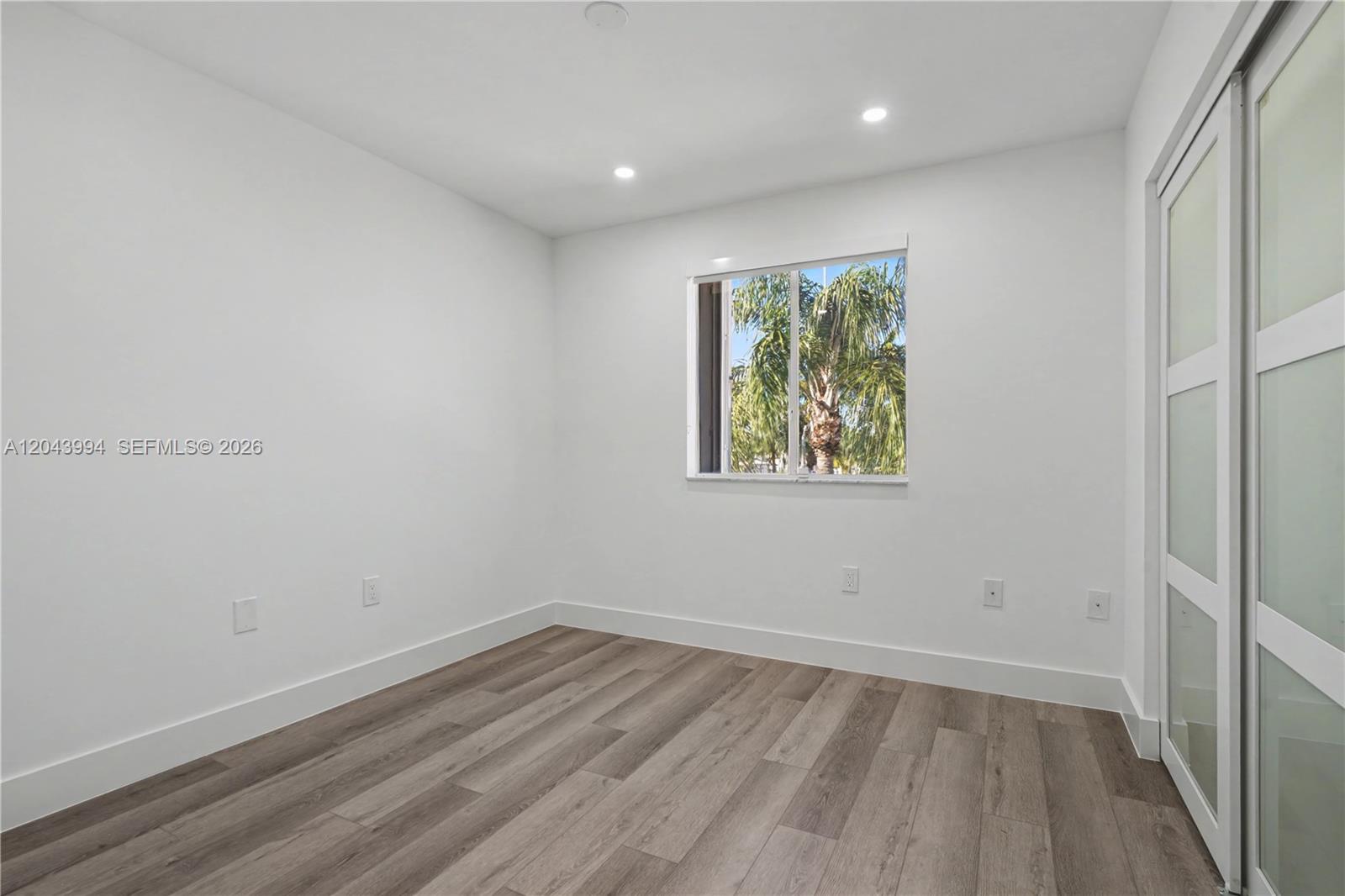 A minimalist bedroom features white walls, wood-look flooring, recessed lighting, and a sliding glass door — 16240 SW 75th St # 0, Miami FL 33193, MIAMI, FL